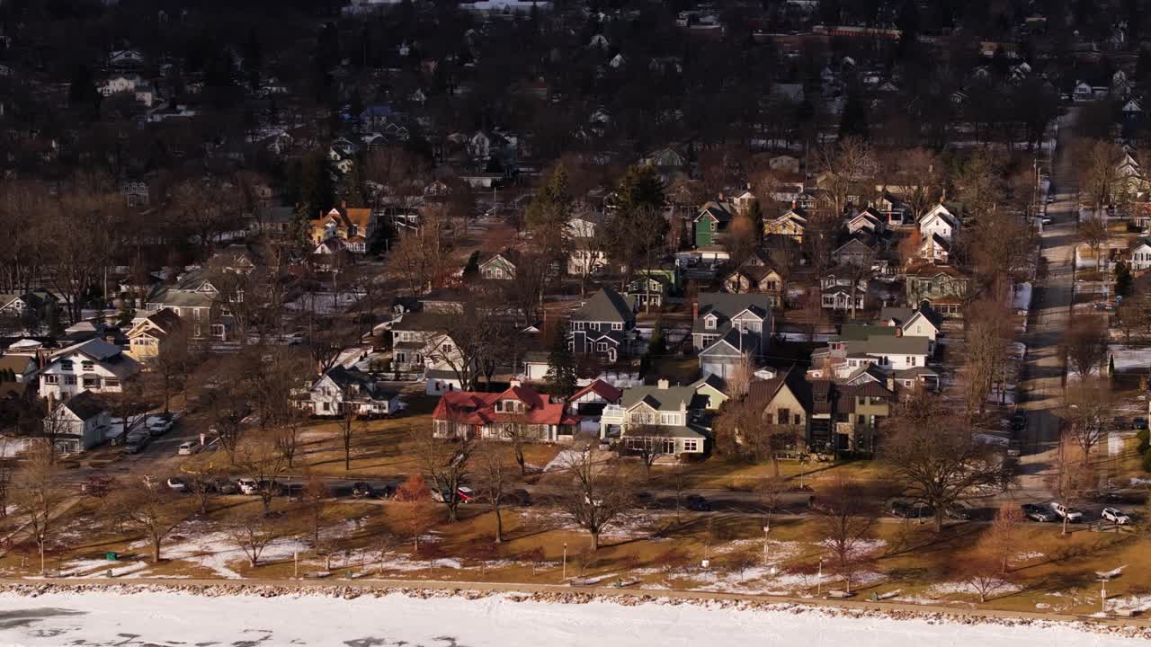 Icy frozen lake shoreline and suburban homes in winter, low warm light on rooftops, aerial establishing dolly