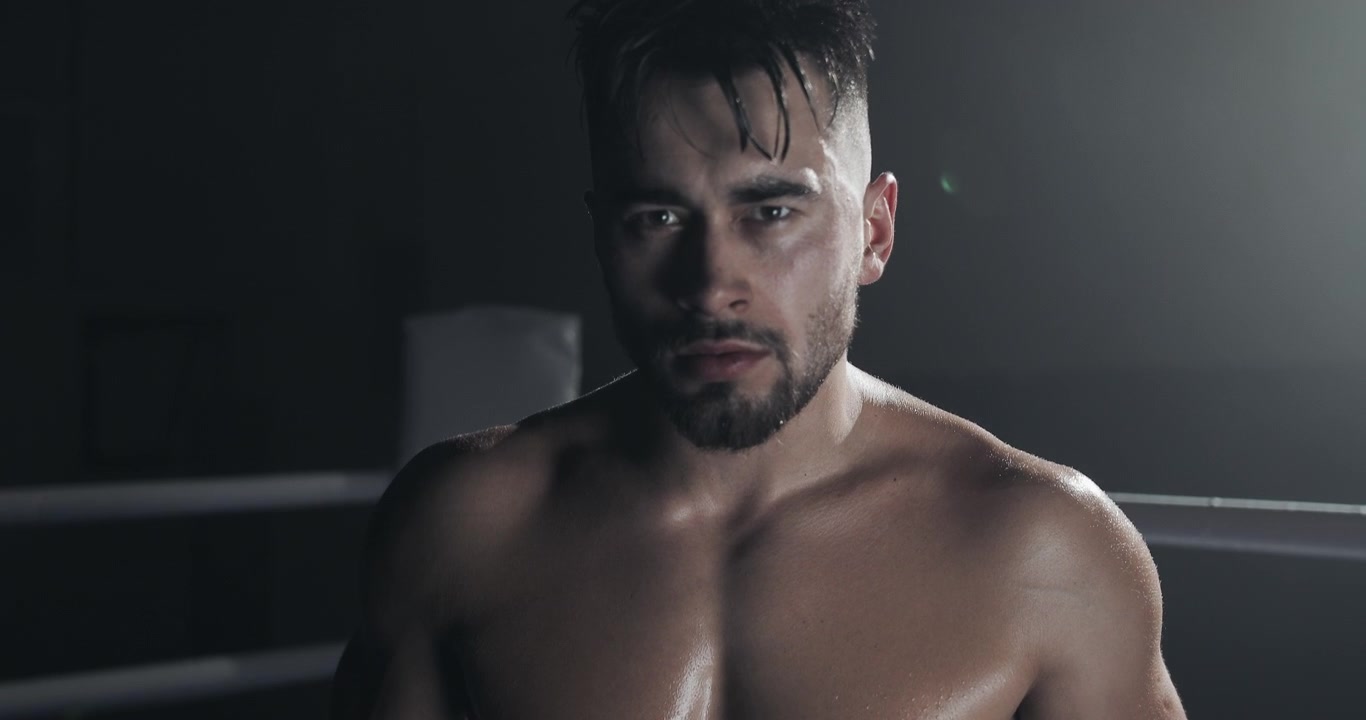 Pugile muscoloso con sguardo intenso in un ring di pugilato buio.