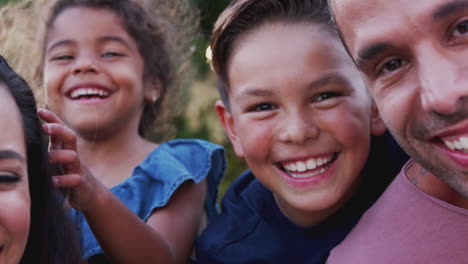 portrait of smiling hispanic family with parents giving children piggyback rides in garden at home