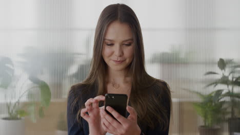 retrato de una joven ejecutiva independiente de negocios que usa un teléfono inteligente disfrutando de los mensajes de texto navegando por mensajes en línea enviando correos electrónicos sms en el teléfono móvil en la oficina