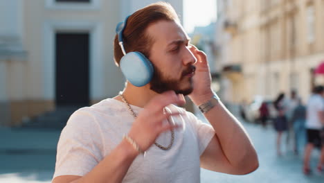 happy young man guy in wireless headphones choosing listening music dancing outdoors city street