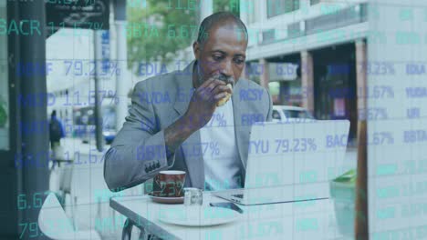 stock market data processing against african american senior man having a snack while using laptop