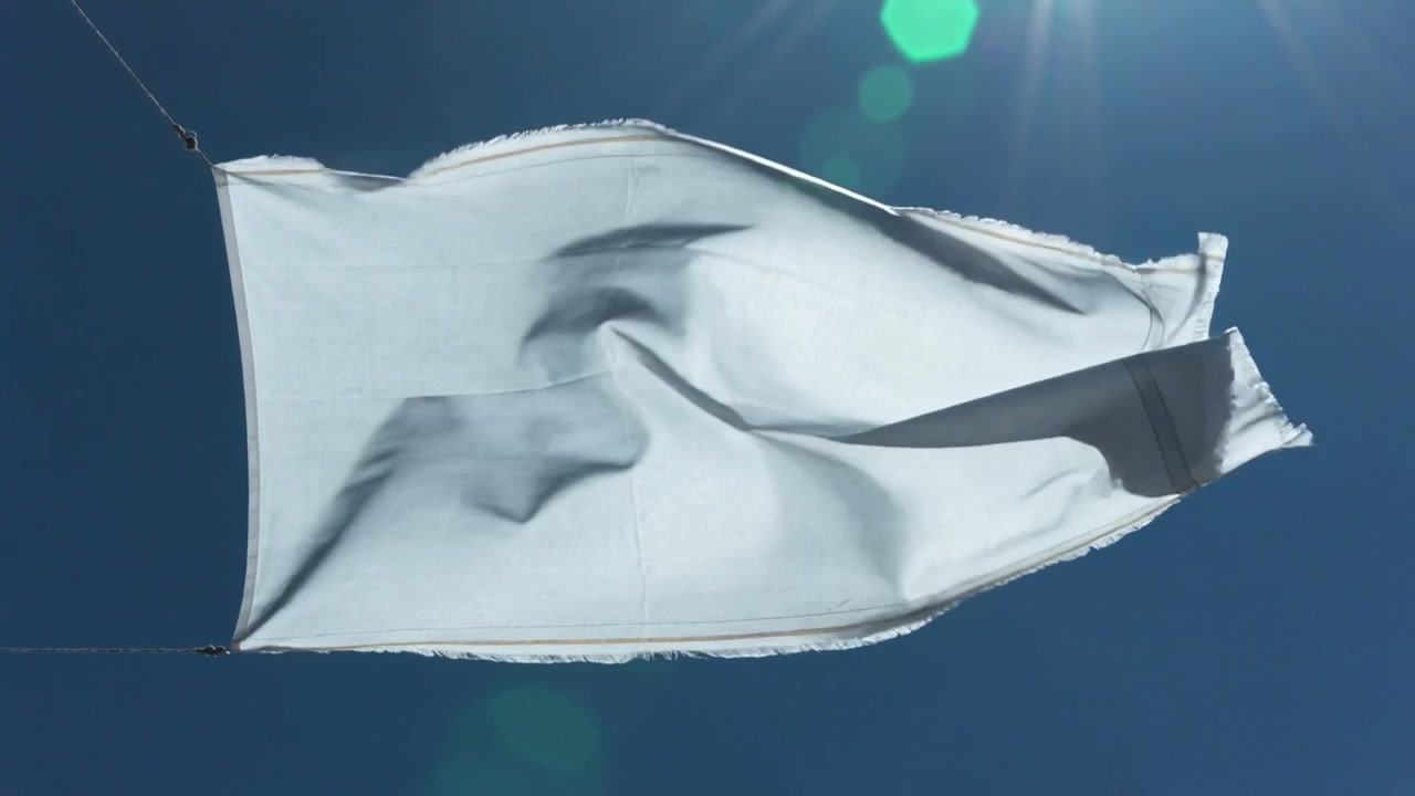 Una raffica di vento solleva un panno bianco con orlo sfilacciato e mollette, che ondeggia e si agita sui fili stendibiancheria sul tetto.