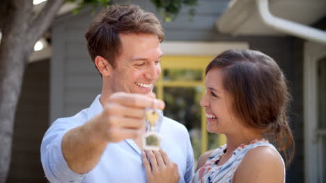 portrait of happy couple standing outside new home with keys