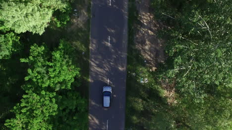 Top-view-car-driving-on-asphalt-road-past-green-trees-countryside