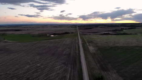 Tilt-up-aerial-view-of-a-countryside-road-with-agricultural-fields-around-at-sunset