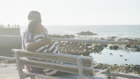 Happy-senior-african-american-couple-sitting-on-bench-on-promenade-by-the-sea,-slow-motion