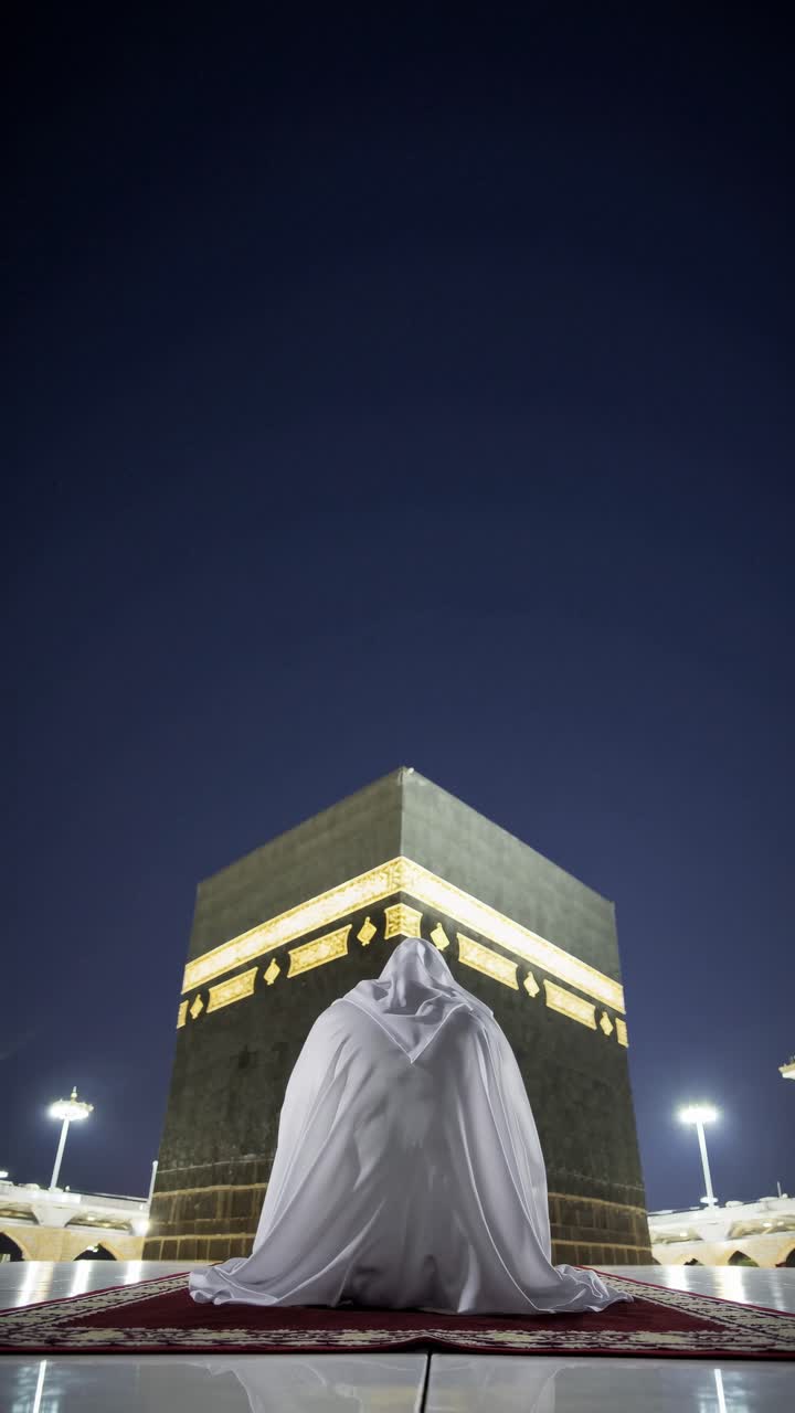 A low-angle shot captures a person in white facing the Kaaba at night, evoking a serene, spiritual