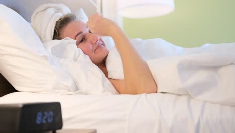a relaxed woman wrapped in a towel stretches in bed as the morning alarm signals the start of a new. a relaxed woman wrapped in a towel stretches in bed as the morning alarm signals the start of a new day