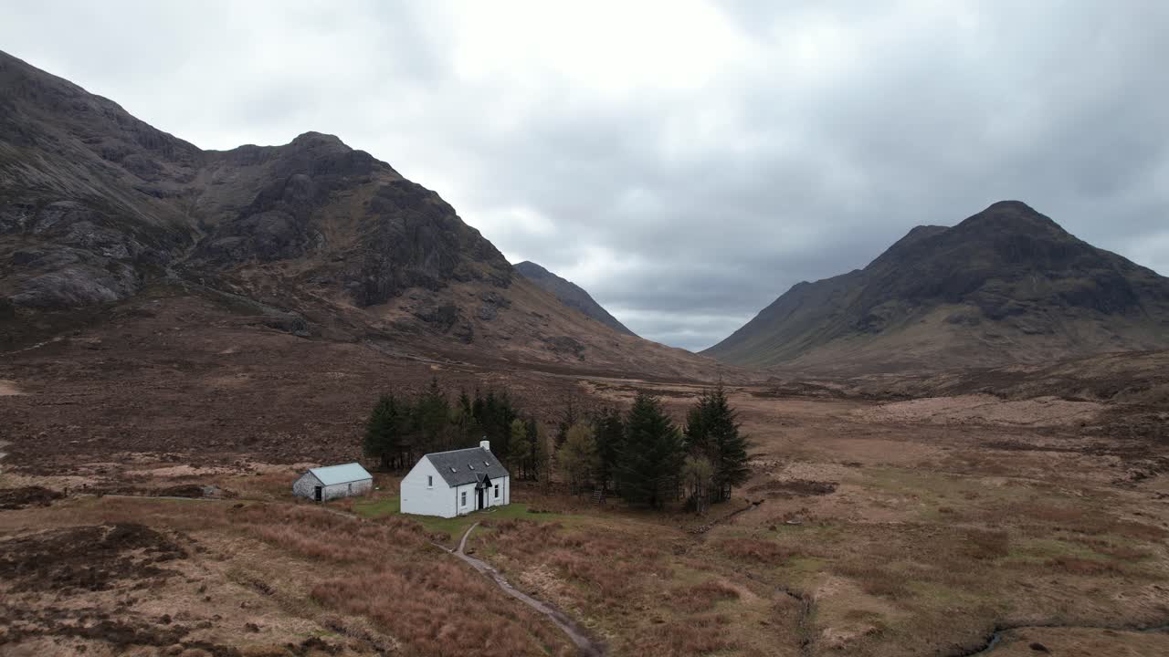 Cinematic orbit panoramic drone shot of Glencoe Highlands with remote white wee cottage in Scotland