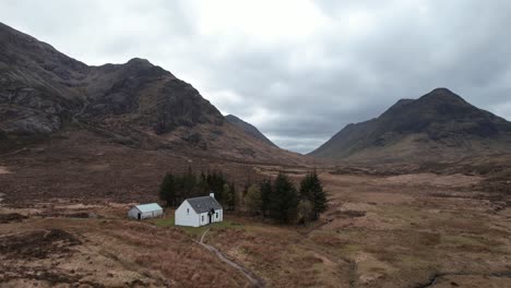 cinematic orbit panoramic drone shot of glencoe highlands with remote white wee cottage in scotland