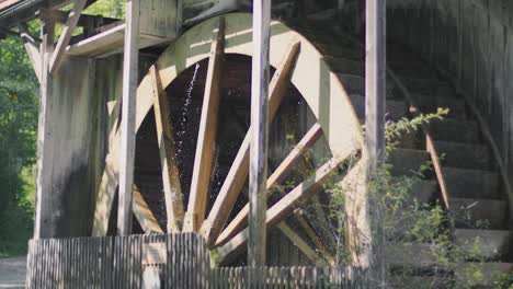 slow motion close up of a gigantic historic ancient wooden water wheel of a watermill spinning while water is flowing on it, splashing it around