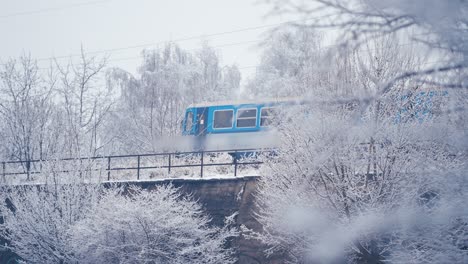 a small two-carriage local train passes on the bridge through the snowy winter landscape