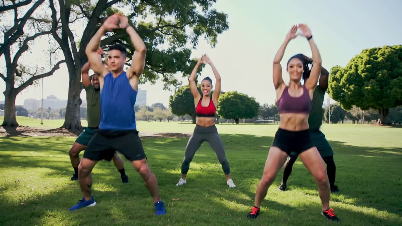 Un grupo de fitness realiza sentadillas sincronizadas en un soleado césped de parque, vistiendo camisetas sin mangas y relojes.