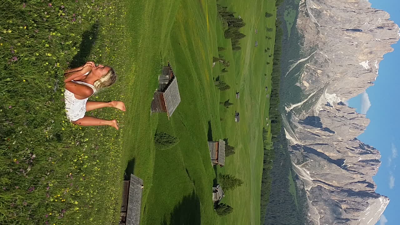 Romantic scene with a beautiful blonde girl lying on a meadow with green grass and flowers in Alpe di Siusi, Dolomite Mountains, Italy