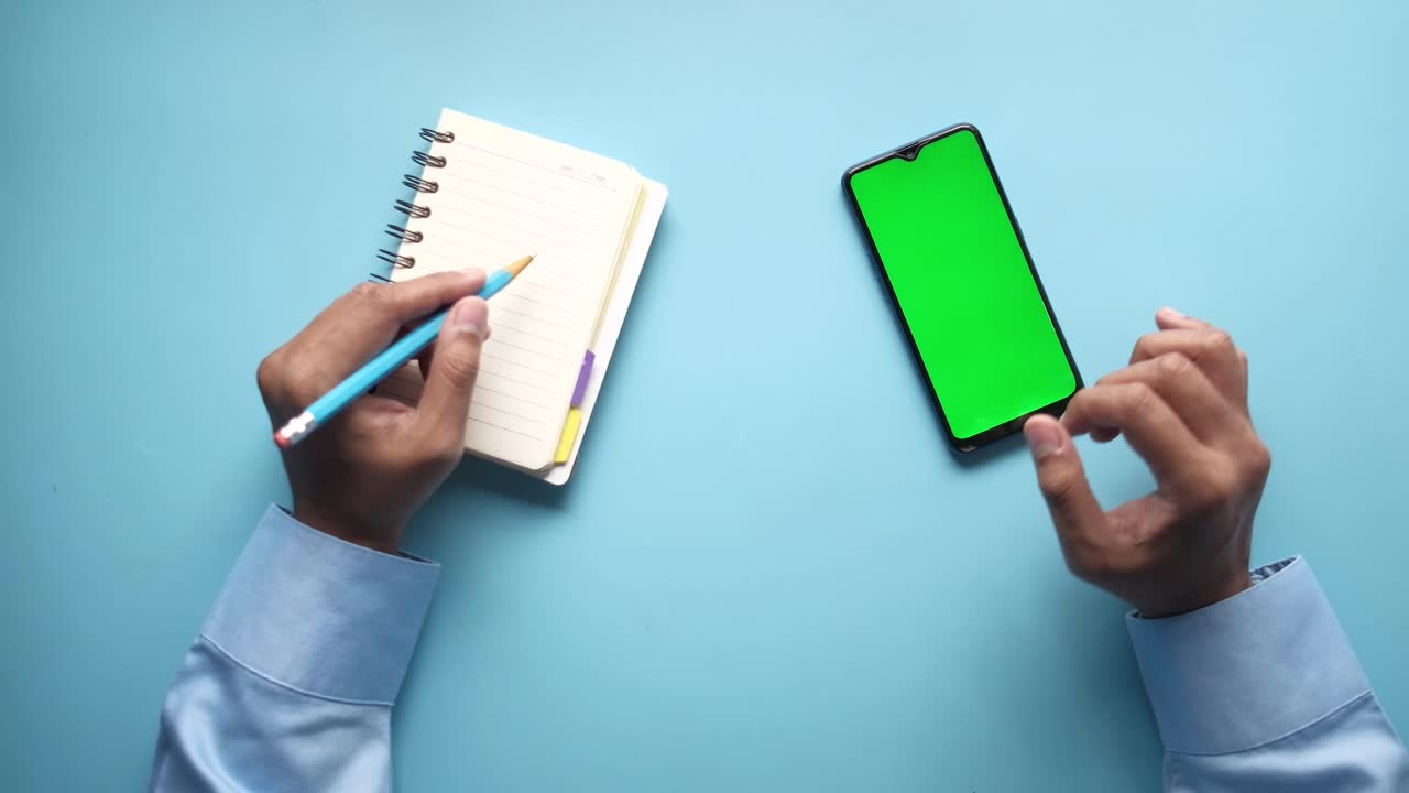 Man writing in notepad and using smartphone with green screen
