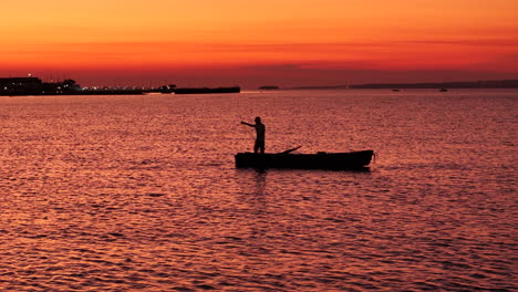 Backlit-panoramic-shot-of-a-fisherman-at-sunset-in-a-canoe-in-EL-Brete-Bay-in-Posadas,-Argentina