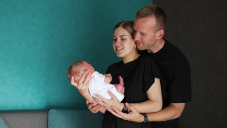 caucasian parents waving their newborn indoors. man and woman in black t-shirts smiling to their baby.
