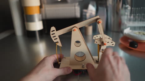 hands building a wooden model of an oil pump