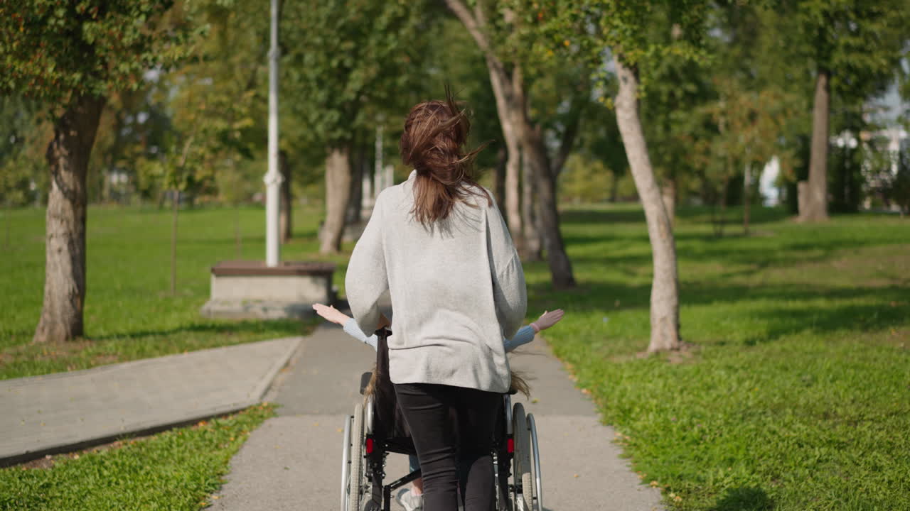 Kvinne dytter datter med skade i rullestol i parken.