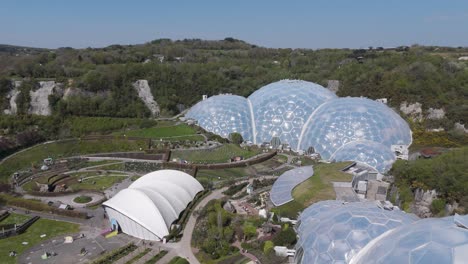 broad aerial panorama of eden project dome clusters shimmering above concentric gardens and forested slopes, illustrating regeneration, biodiversity and renewable innovation