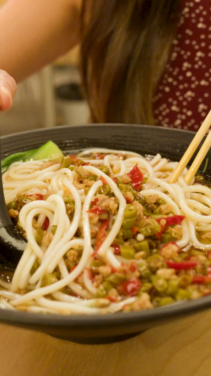 Close-up de mulher mexendo sopa de macarrão picante com bok choy, pimenta e carne moída.