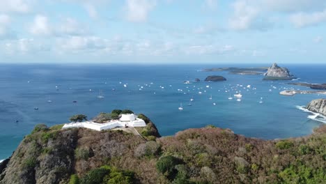 forward movement with drone on the island of fernando de noronha, lighthouse and boats in the background, blue sky and sunny day