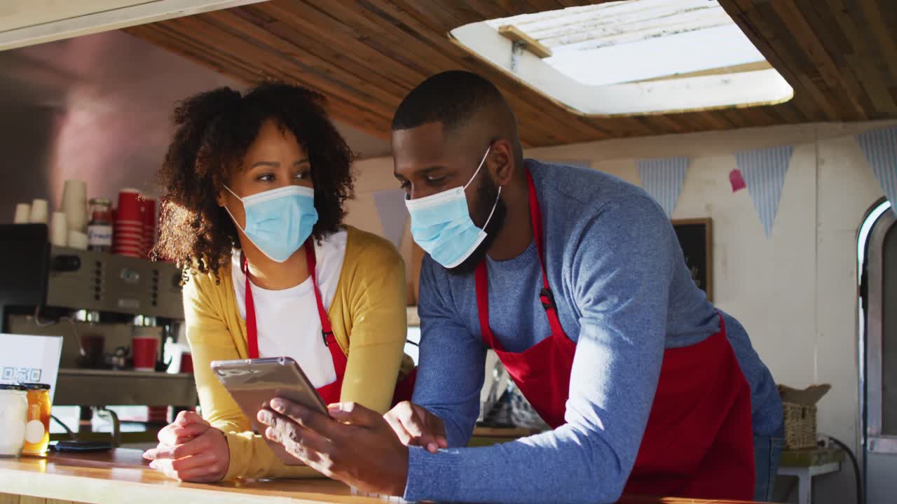 African american couple wearing face masks using digital tablet in the food truck