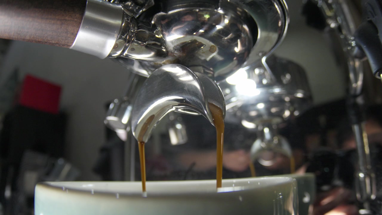 Primo piano di espresso che scorre dal portafiltro della macchina nella tazza in un ambiente da caffè
