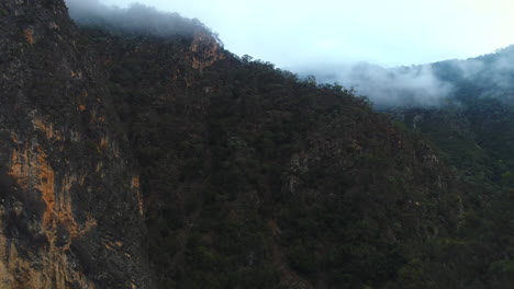 Dron-Aéreo-Que-Revela-Enormes-Montañas-Rocosas-Cubiertas-De-Una-Espesa-Tierra-De-Arbustos-Australianos-En-Una-Brumosa-Mañana-De-Invierno-En-El-Parque-Nacional-Bungonia-Nsw-Australia