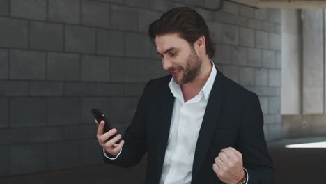 Portrait-of-excited-business-man-reading-good-news-on-smartphone-at-urban-street