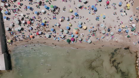 imágenes aéreas de arriba hacia abajo alejándose de los turistas en la playa con una variedad de colores en bari, italia con las olas del mar moviéndose