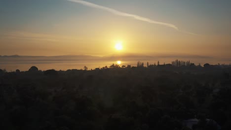 aerial over silhouetted landscape with golden yellow sunset over lake. follow shot