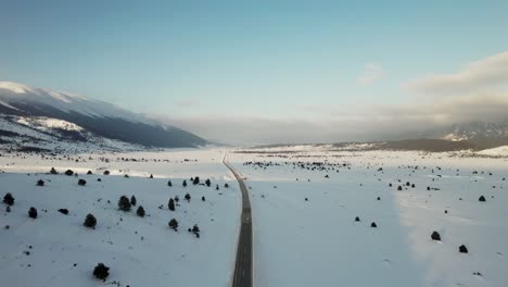 an endless road winding through a snowy landscape, the road stretches far ahead, disappearing into the horizon, while the snow-covered peaks of the mountains loom majestically in the background