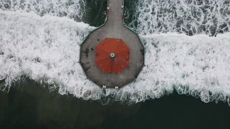 California-Historical-Landmark-called-Roundhouse-Aquarium-at-the-end-of-the-pier-at-Manhattan-Beach-and-visitors,-view-down-from-the-drone