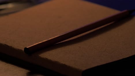 vintage pencil with light brown notepad on the wooden desk, harsh shadows from warm white light, minimal retro interior decoration concept, calm evening or night feeling, closeup shot