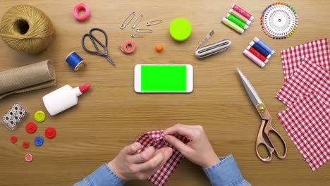 overhead shot of woman sewing plaid fabric by smartphone