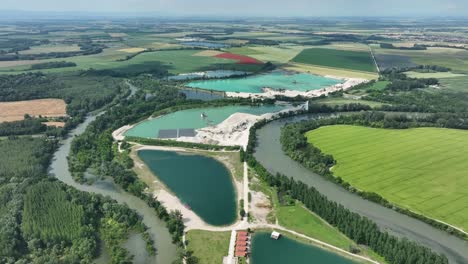 Die-Drohne-Schwebt-über-Dem-Kleinen-Fluss-Donau-Und-Erfasst-Kiesgruben-Und-Seen,-Während-Sich-Wechselnde-Wolkenschatten-Auf-Dem-Wasser-Darunter-Tanzen