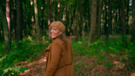 Caucasian-women-with-an-overcoat-and-hat-walking-in-the-forest-trail-waving-hand-posing-for-the-camera