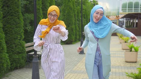 two positive expressive attractive muslim young woman in traditional scarf dancing in the park close up