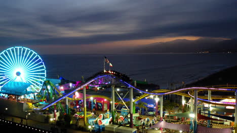 santa monica pier at dusk with illuminated ferris wheel and roller coaster