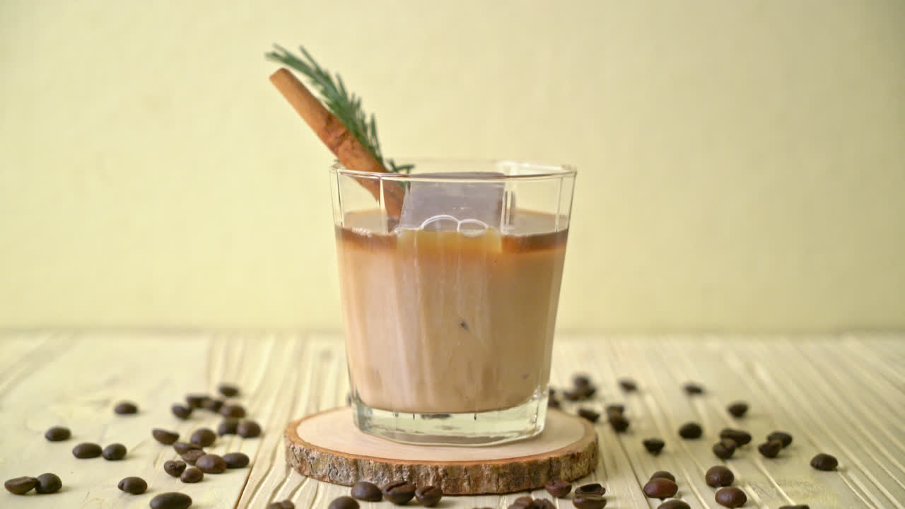 나무 배경에 아이스 큐브, 계피, 로즈마리와 블랙 커피 잔에 우유를 붓는