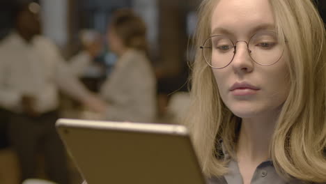 close up of a serious blonde businesswoman with glasses using tablet and working in the office