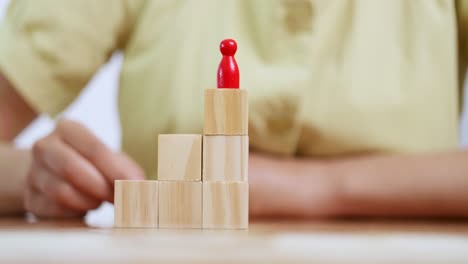 a person carefully places a red figure atop wooden blocks symbolizing growth and achievement