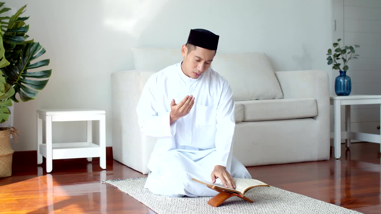 이슬람 옷을 입은 젊은 이슬람 남자가 꾸란을 읽고 기도하고 있습니다.