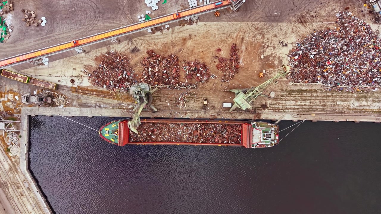 Grande nave da carico attraccata in un porto che carica rottami metallici da un sito di riciclaggio alla luce del pomeriggio.