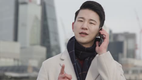 young asian businessman talking on mobile phone with london city skyline in background