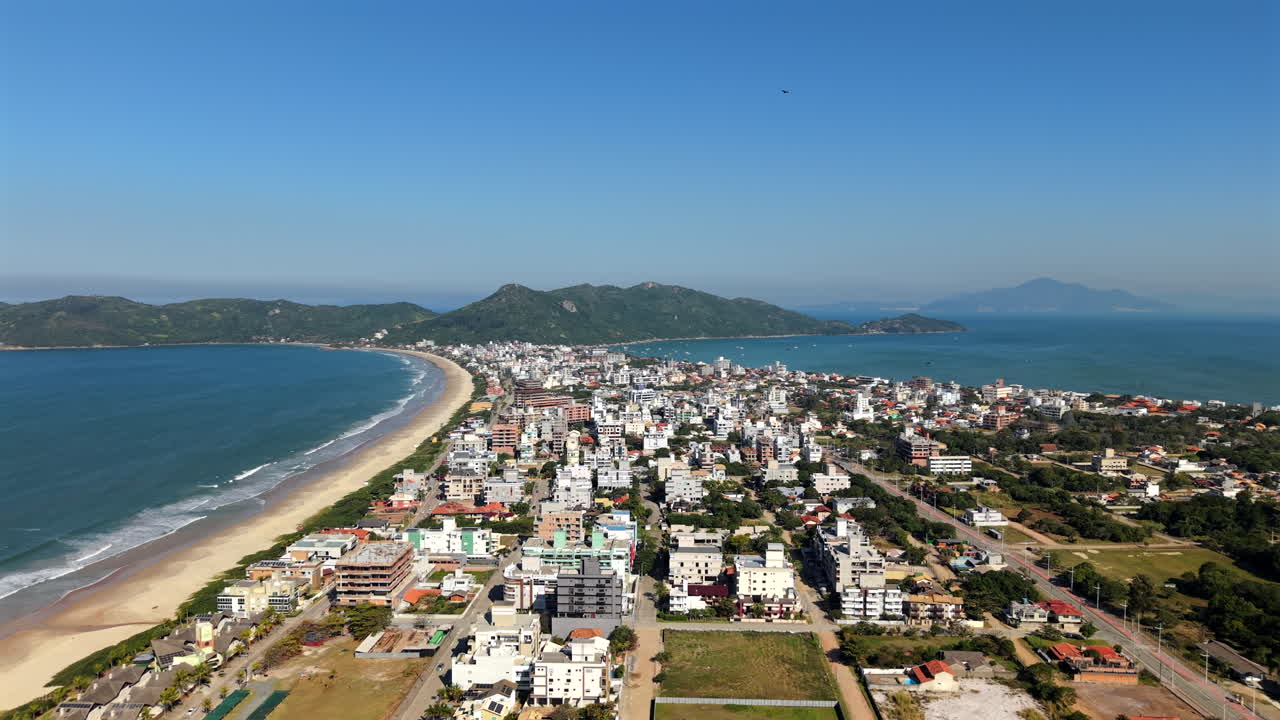 Panoramic drone fly over the Mariscal long sandy coastline with residential area, Canto Grande, Santa Catarina, Brazil