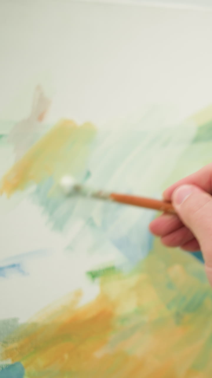 A close-up of an artist's hand, clad in a checkered shirt, as it skillfully paints a colorful portrait on a canvas. The scene captures the artist s meticulous brushwork, bringing the artwork to life