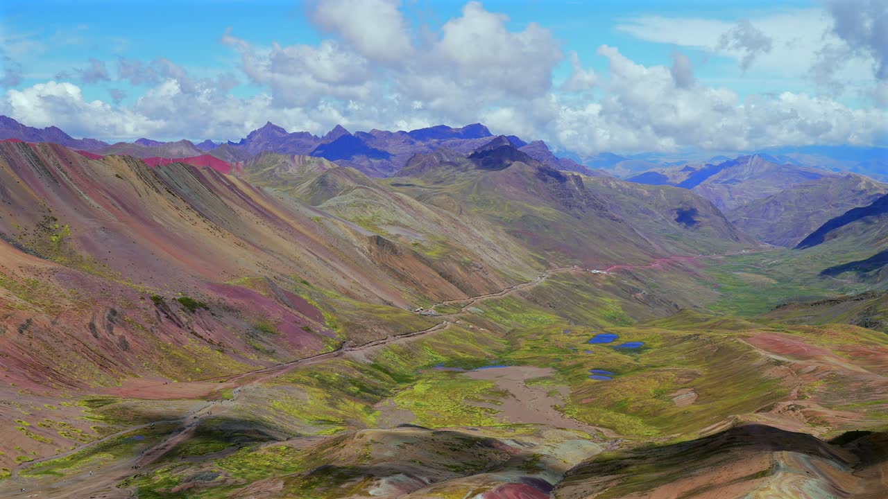Paesaggio mozzafiato della Montagna Arcobaleno Vinicunca nelle Ande peruviane, con panorama della valle accessibile in 4x4, montagne della catena Vilcanota del Perù vicino al ghiacciaio Ausangate e alle calotte di ghiaccio Quelccaya, sotto un cielo azzurro e soleggiato con nuvole mattutine. Panoramica.